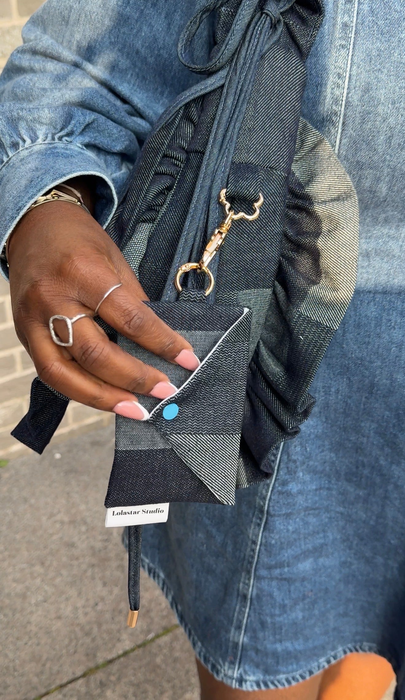 Person holding a denim ruffled crescent bag  with a keychain, wearing a denim dress.
