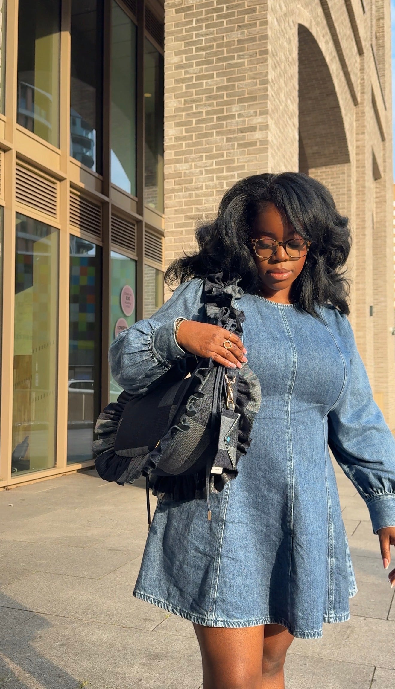 Woman in a denim outfit holding a denim ruffled crescent bag 