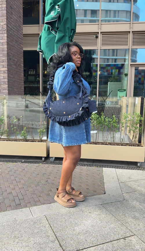 Person wearing a blue denim outfit with a ruffled crescent bag.