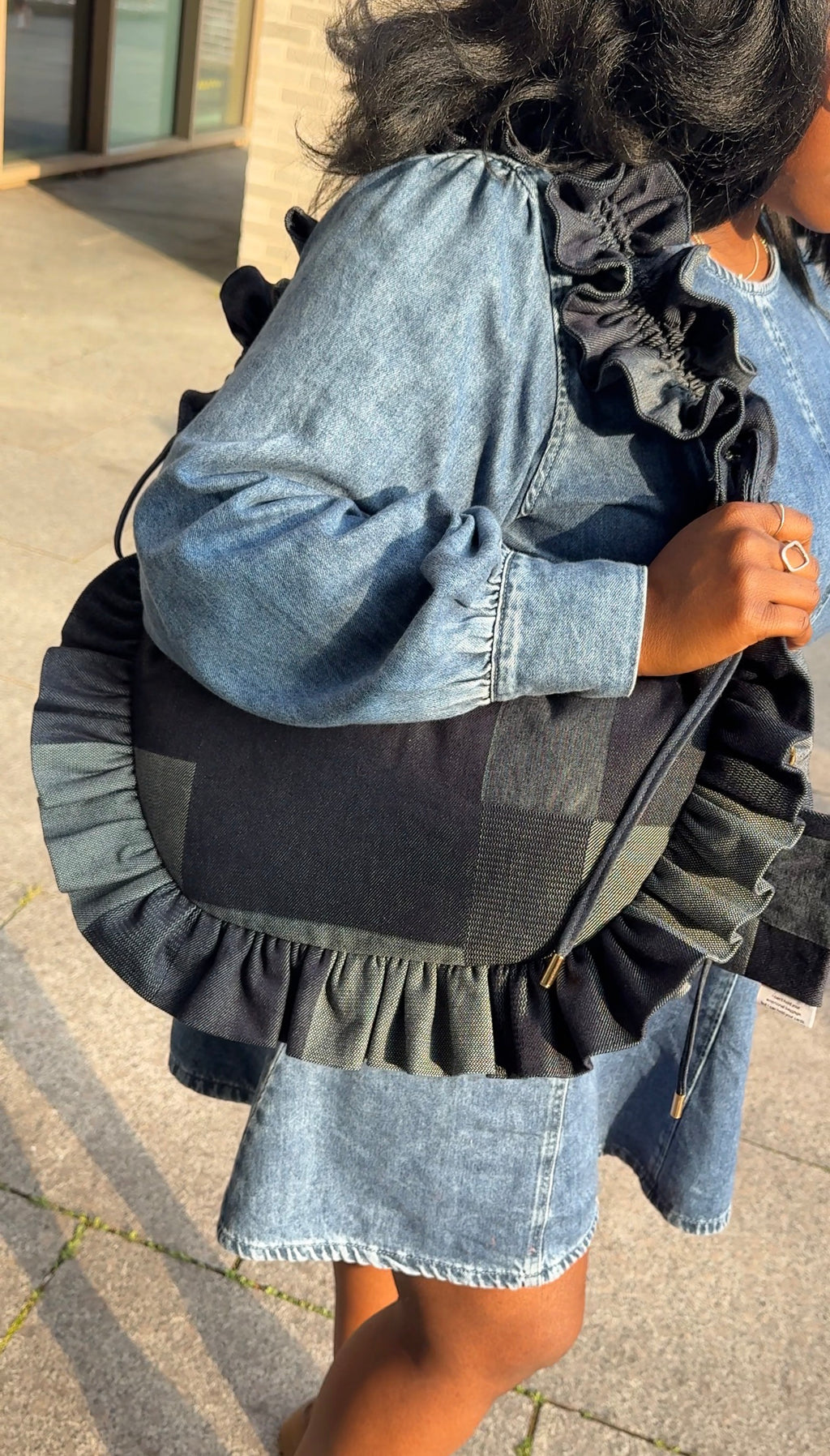 Person wearing a denim dress with a denim ruffled crescent bag 
