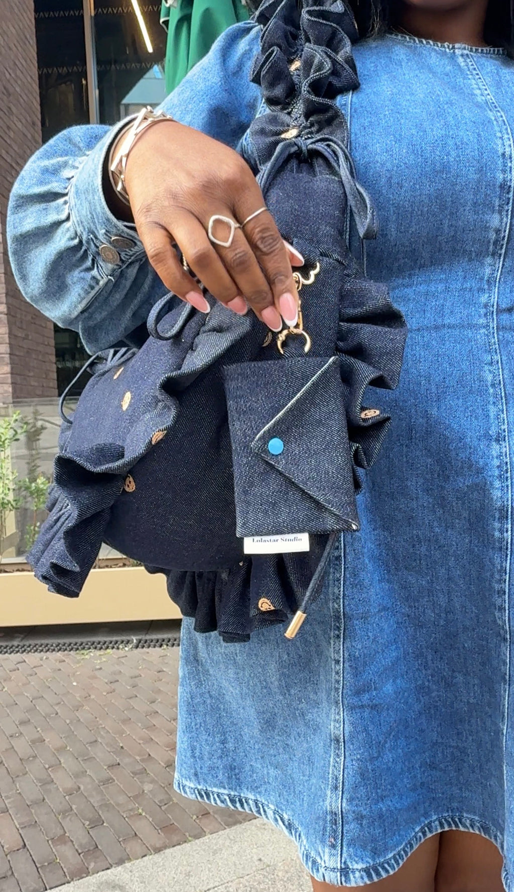 Person wearing a blue denim dress , holding a matching denim ruffled crescent bag and matching card purse
