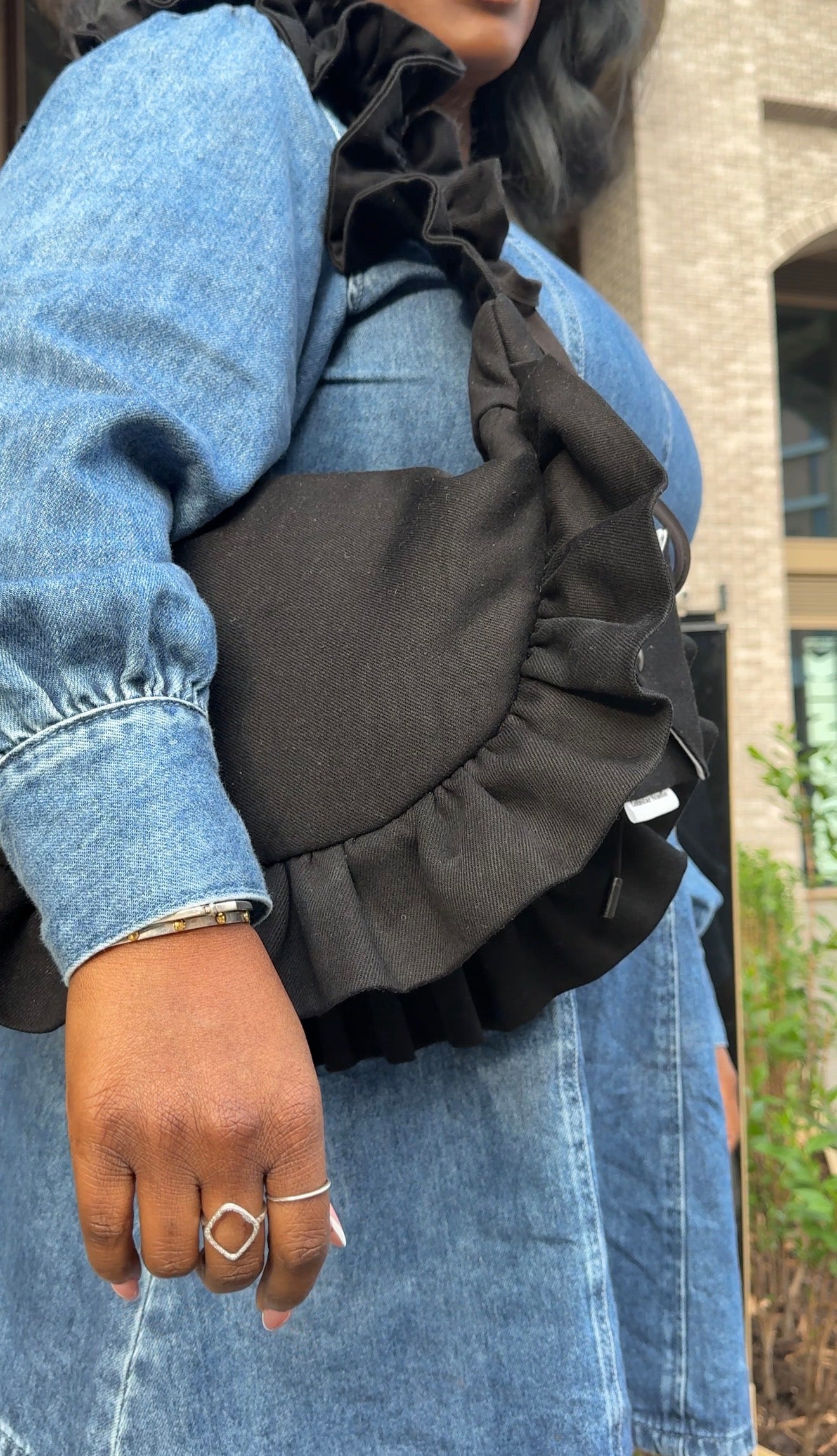 Person wearing a black ruffled handbag with a denim jacket outdoors.