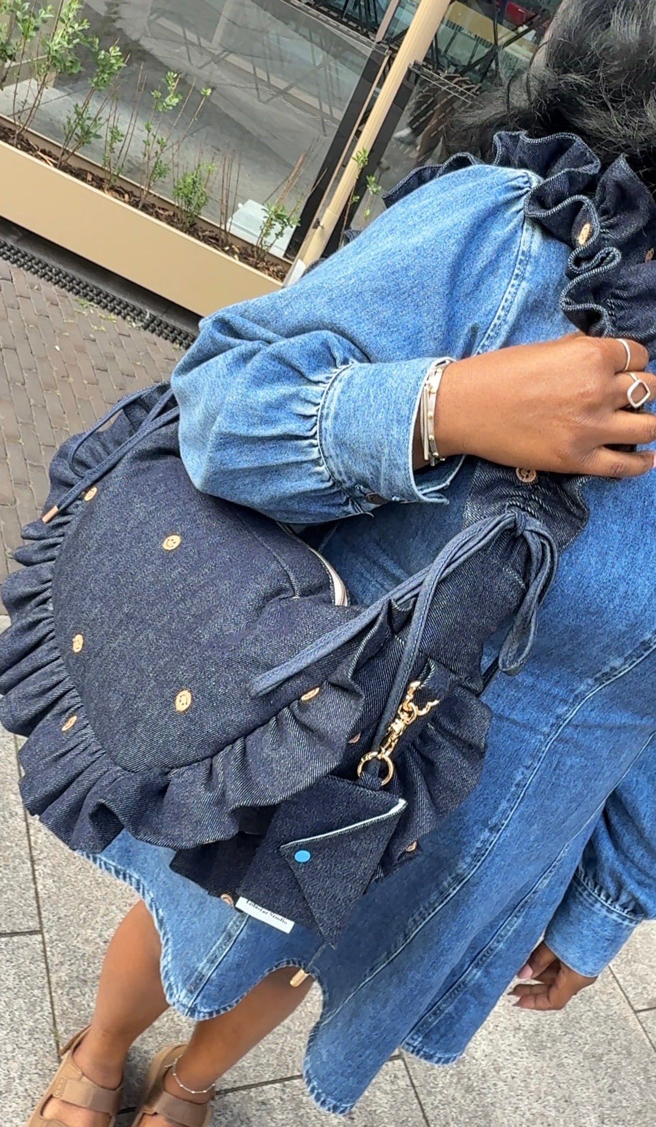 Person wearing a denim jacket with ruffled details, holding a matching denim bag.