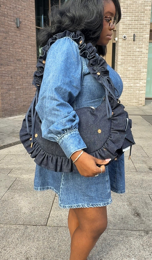 Person wearing a denim dress with a denim ruffled crescent bag  outdoors.