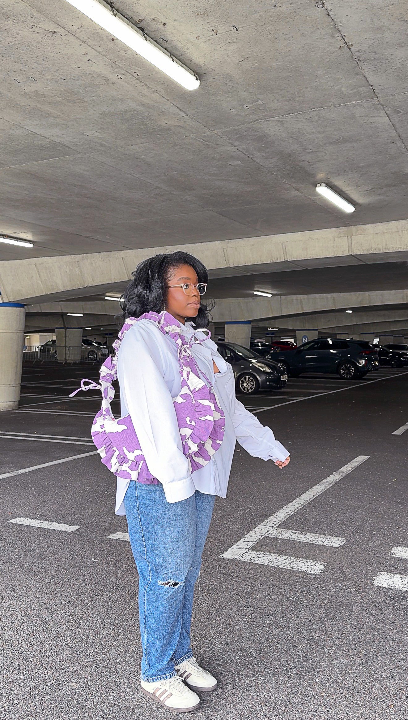 Person holding a purple amethyst cow print ruffled handbag in an underground parking lot