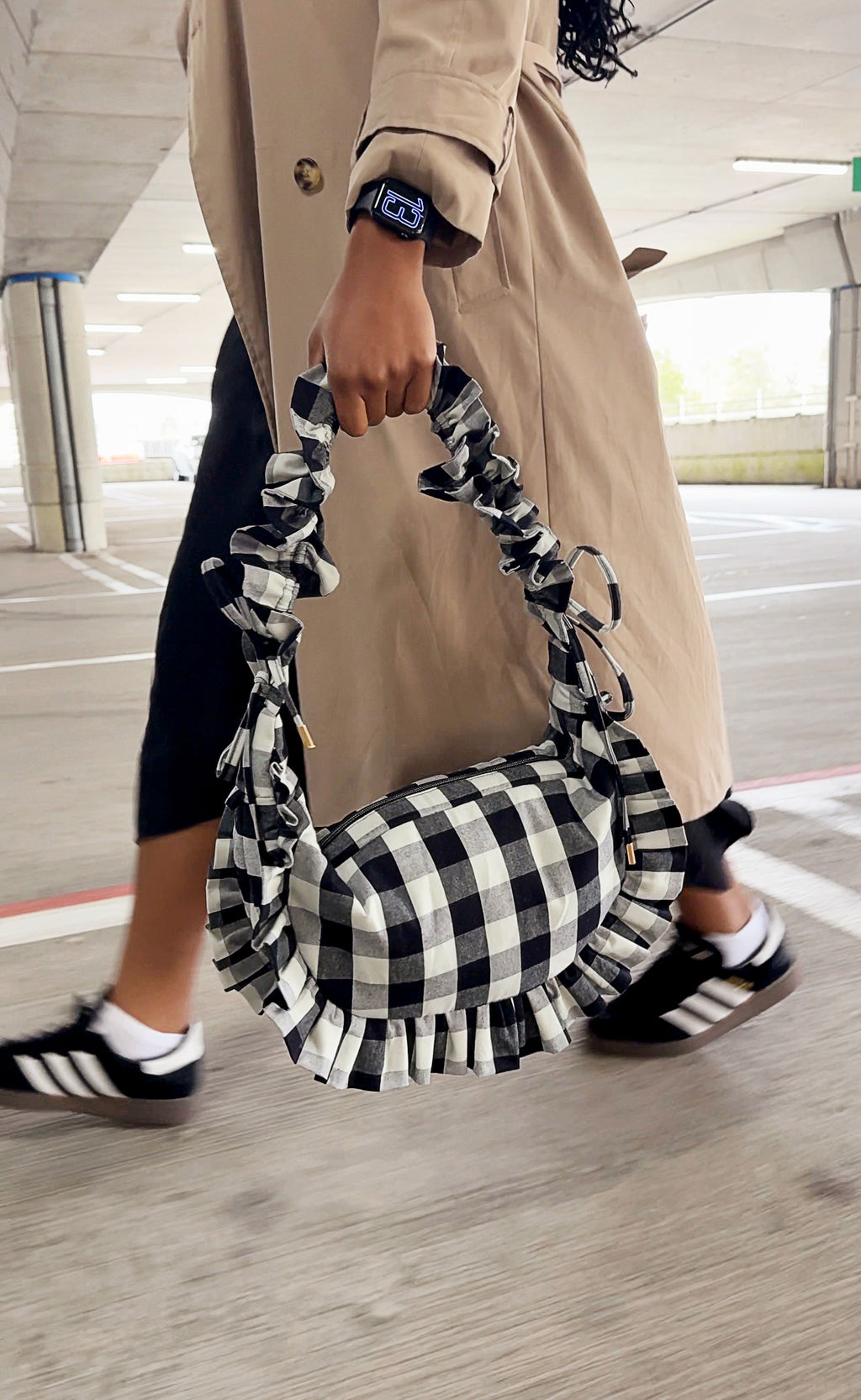 Person holding a black and white checkered ruffle crescent bag in an indoor setting