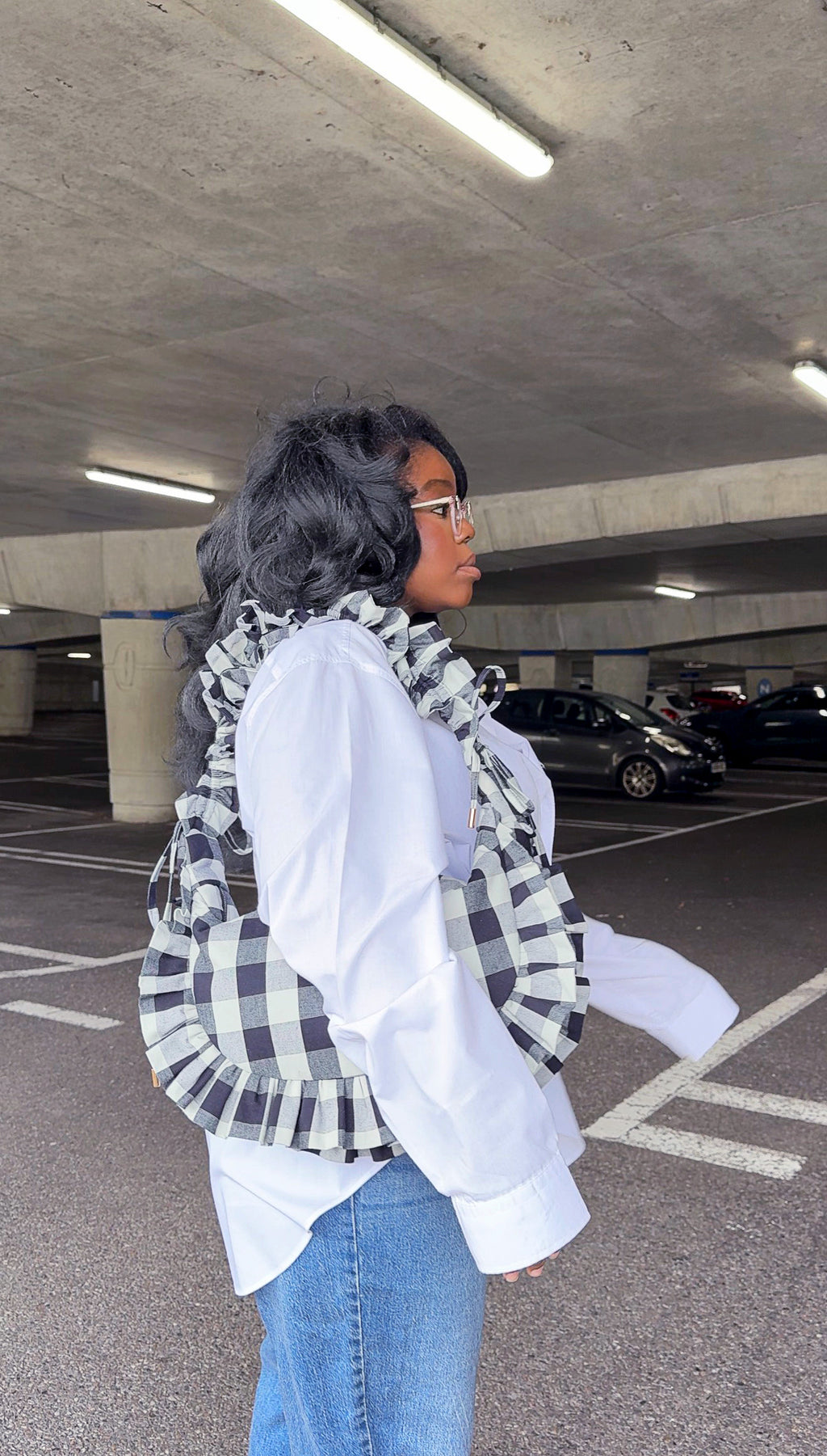 Person holding black and white checkered ruffle crescent bag and  wearing white shirt in an underground parking lot