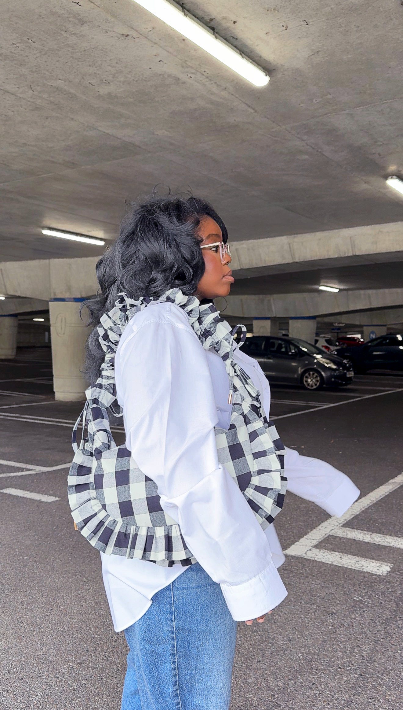 Person holding black and white checkered ruffle crescent bag and  wearing white shirt in an underground parking lot