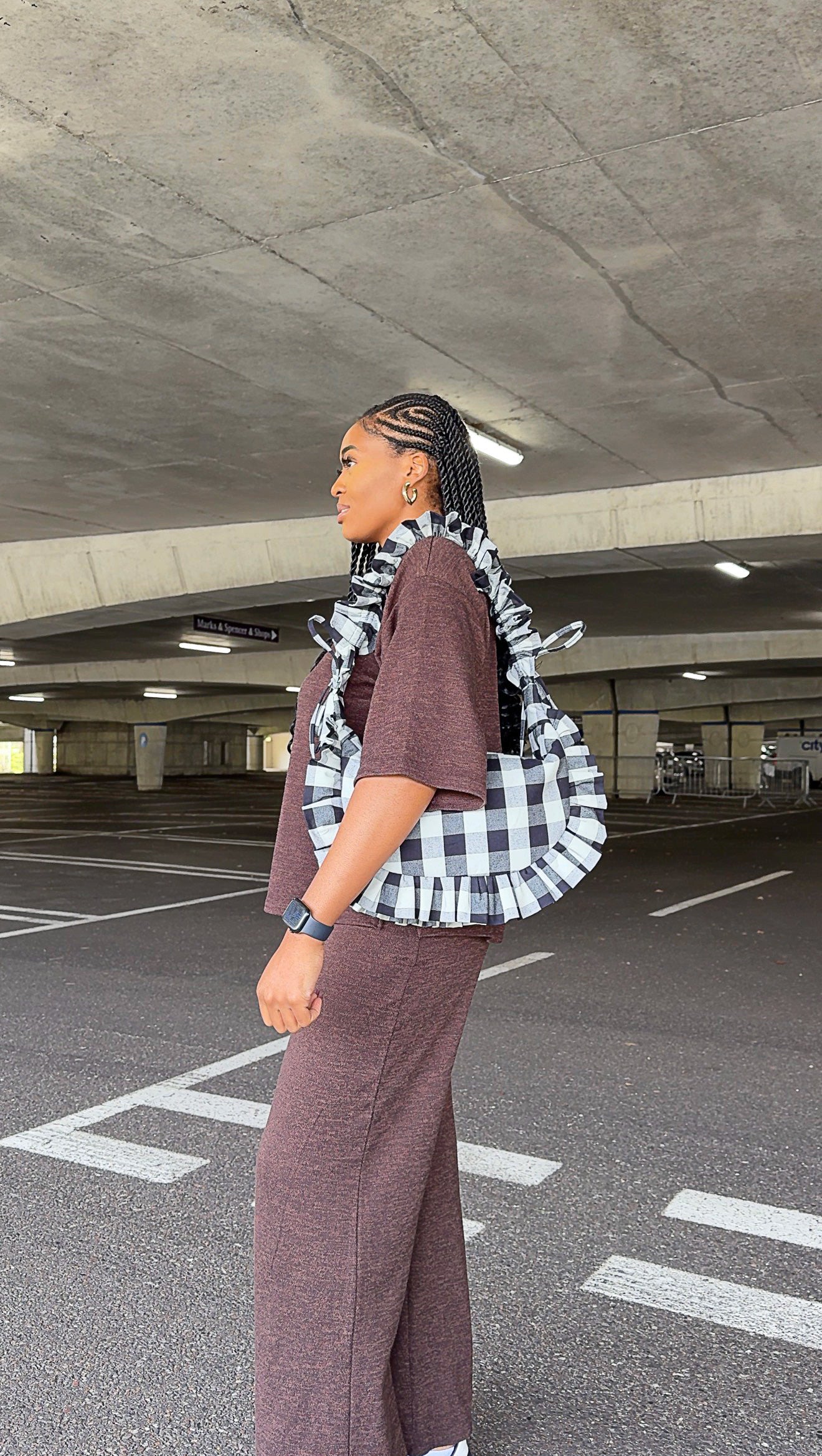 Woman walking in a parking garage carrying a black and white checkered ruffle crescent bag