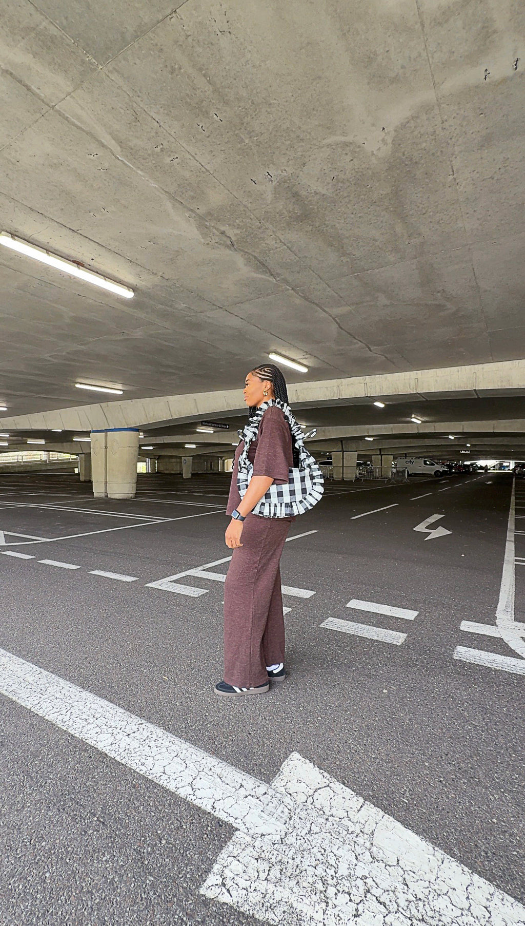Person standing in a parking garage wearing a black and white checkered ruffle crescent bag