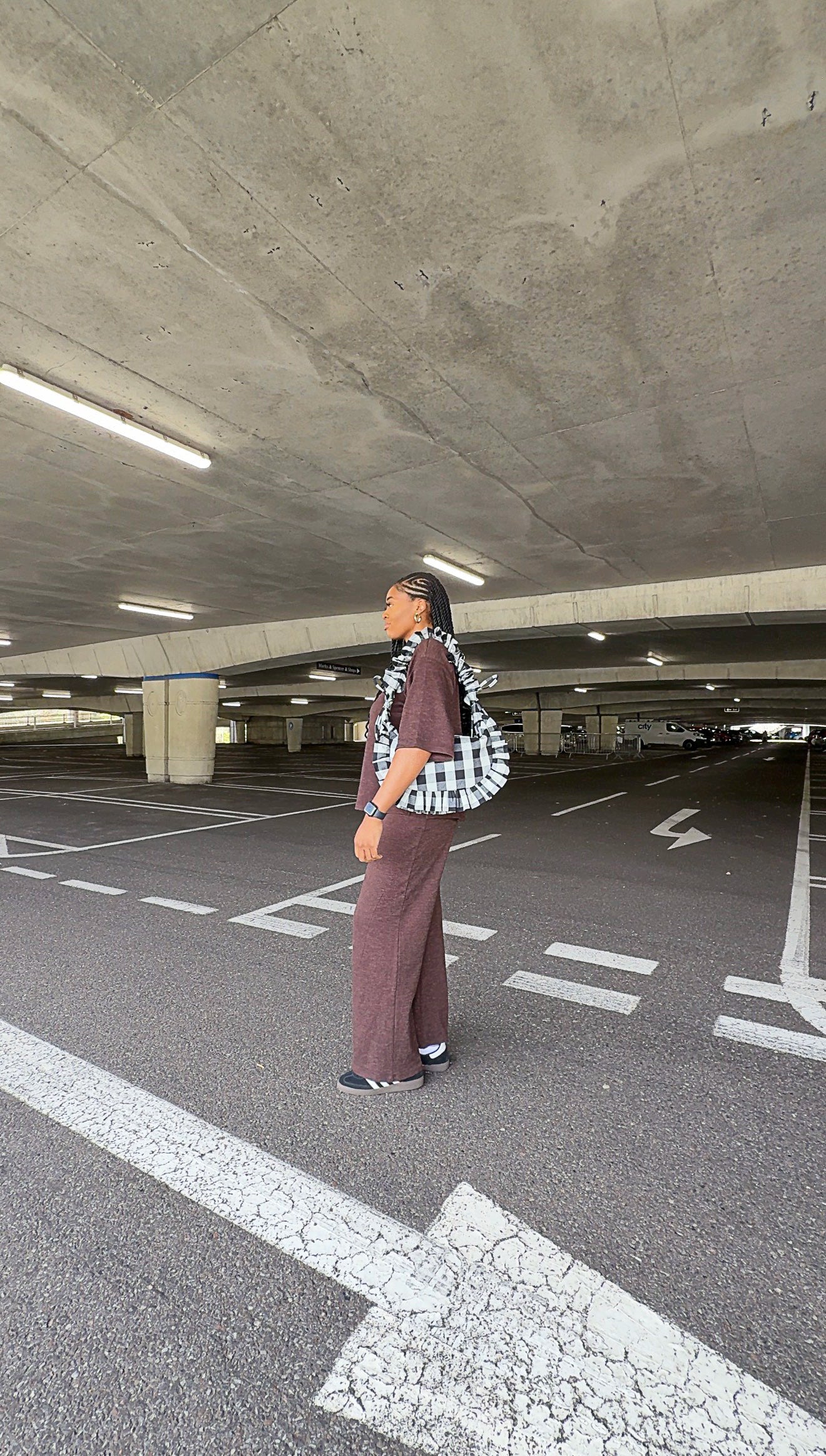 Person standing in a parking garage wearing a black and white checkered ruffle crescent bag