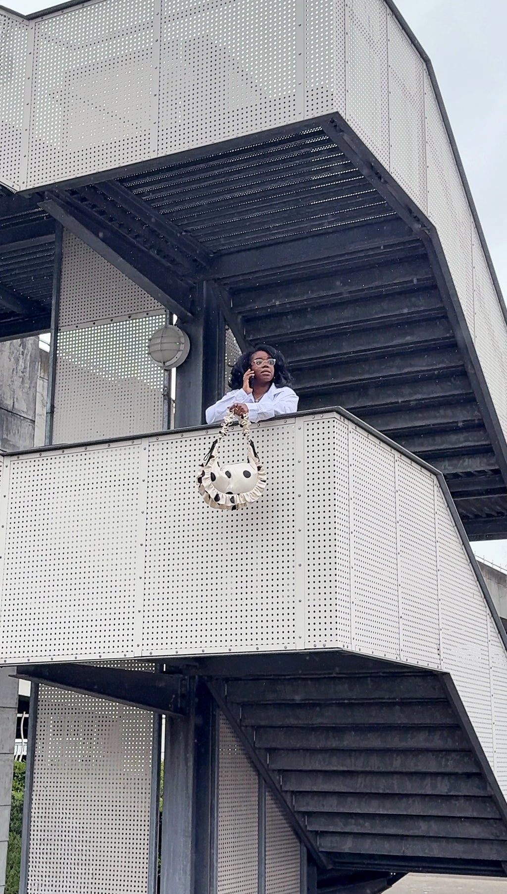 Person sitting on a modern architectural structure holding a white polka dot crescent handbag.