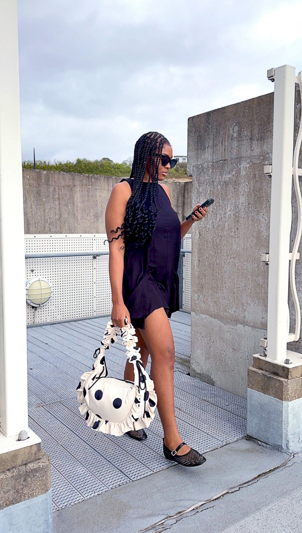 Woman in a dark dress holding a polka dot handbag on a rooftop.