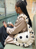 Woman sitting with a ruffled polka dot bag and phone, holding a drink.