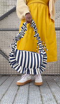 navy and white striped ruffled crescent bag styled with a bright yellow dress and white trainers. 