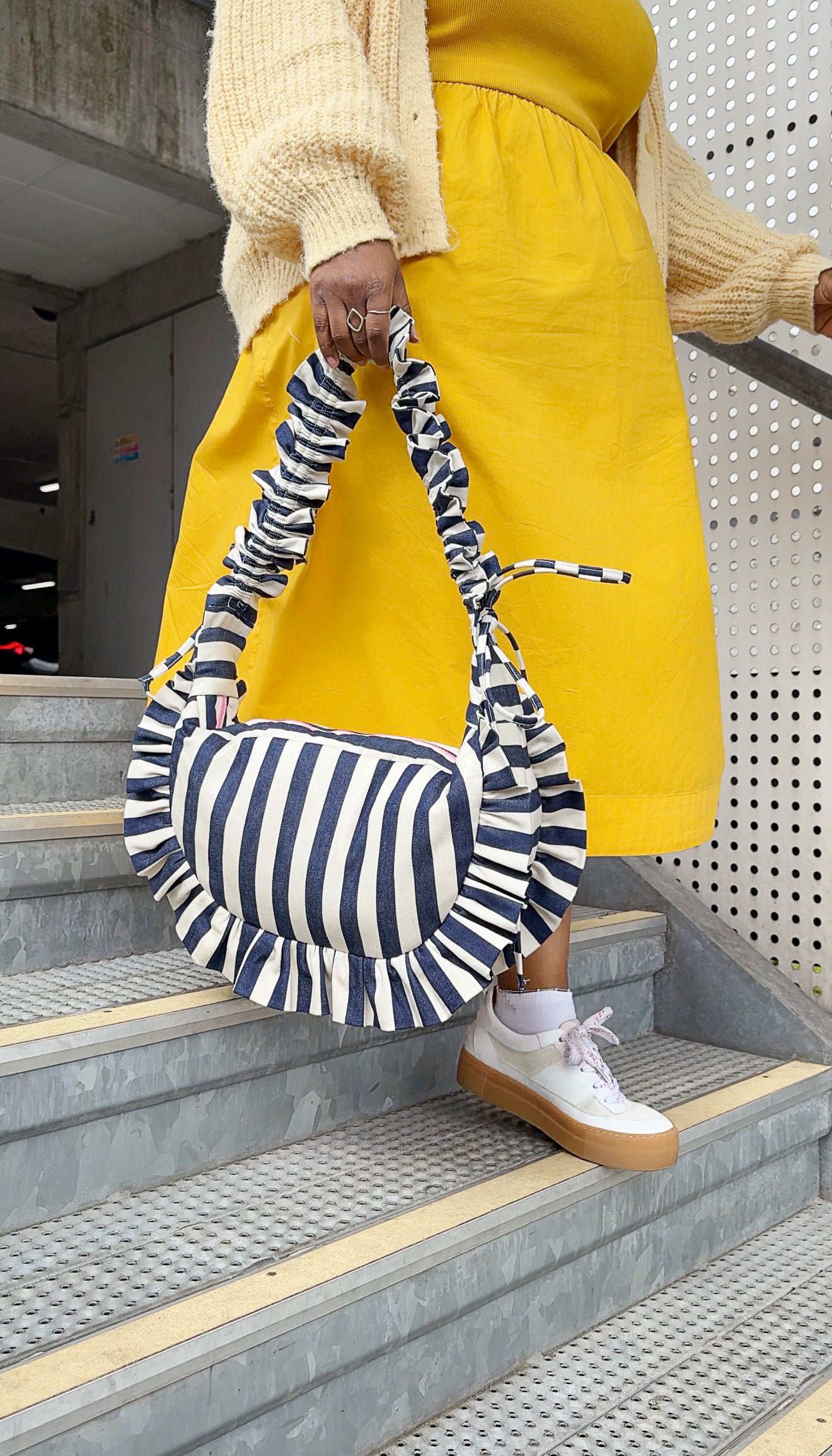 navy and white striped ruffled crescent bag styled with a bright yellow dress and white trainers. 