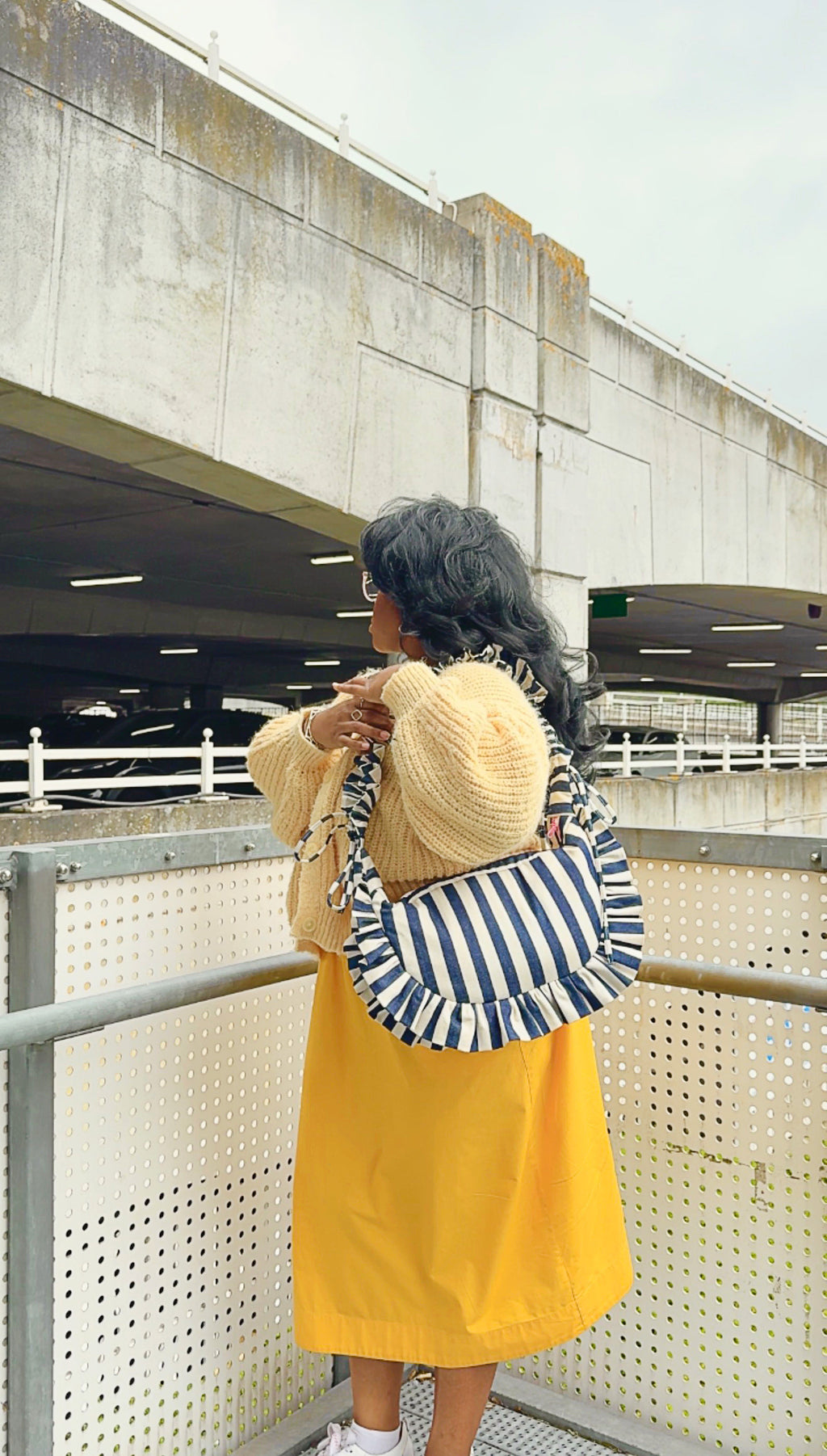 navy and white striped ruffled crescent bag styled with a bright yellow dress and white trainers. 