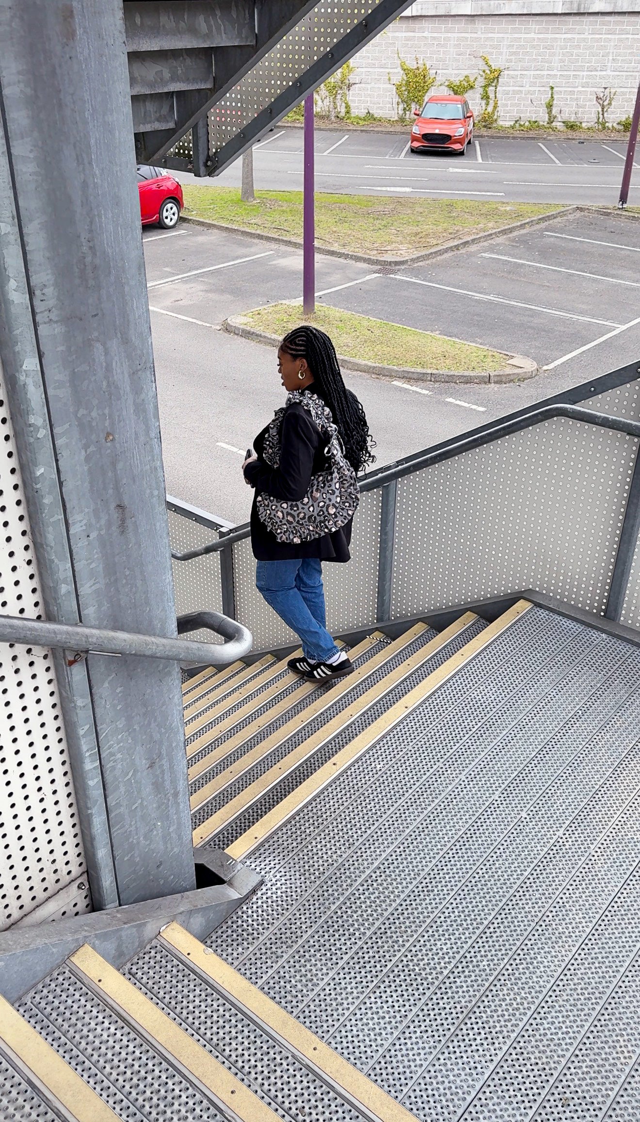 Person walking down stairs in an urban setting with a parking lot in the background slate leopard print ruffled crescent bag.