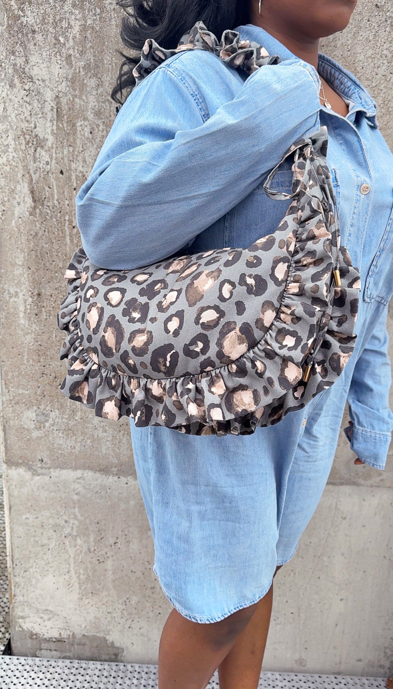 Person wearing a slate leopard print ruffled crescent bag with a concrete wall background