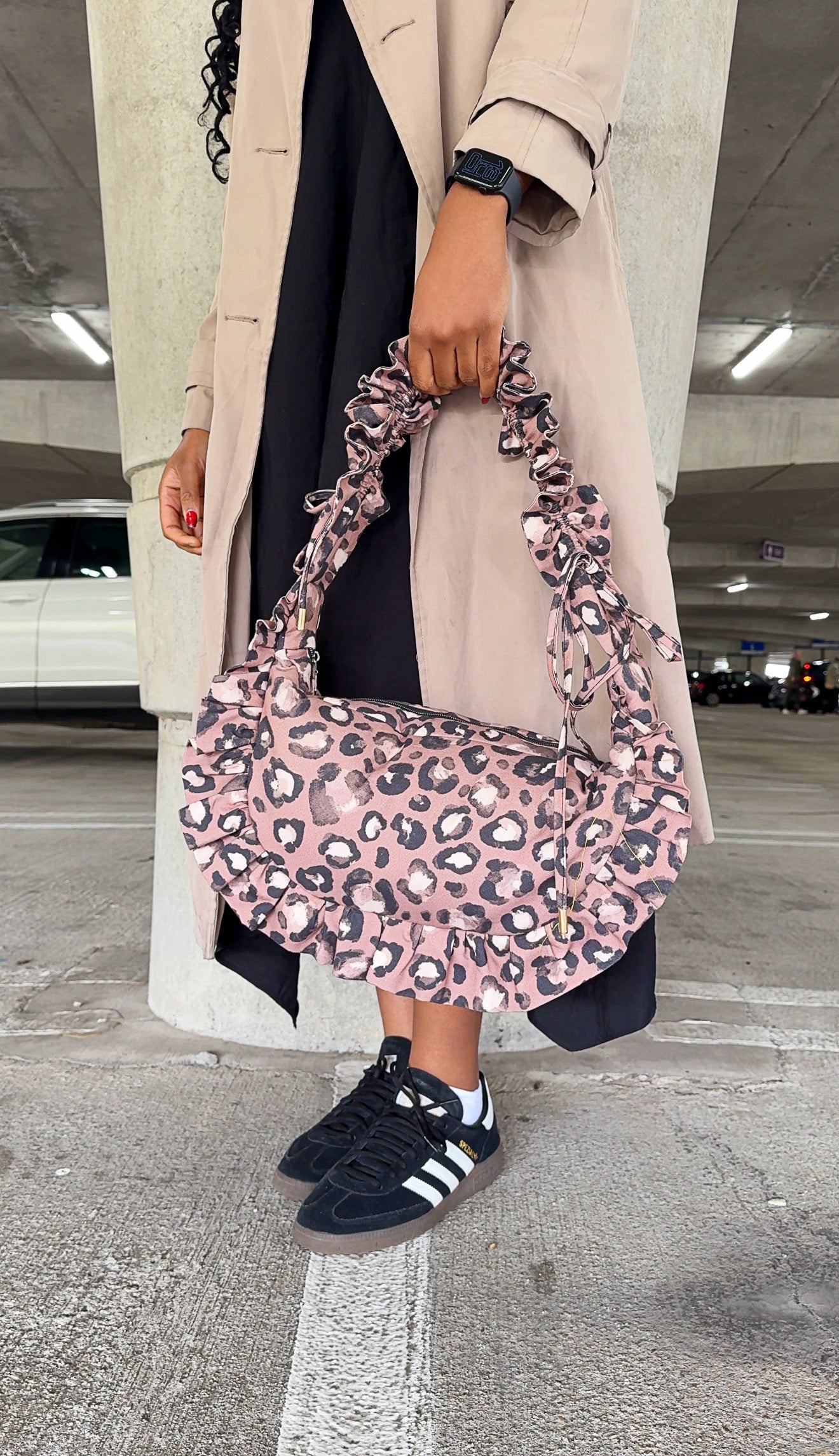 Person holding a taupe brown ruffled crescent handbag in an indoor setting
