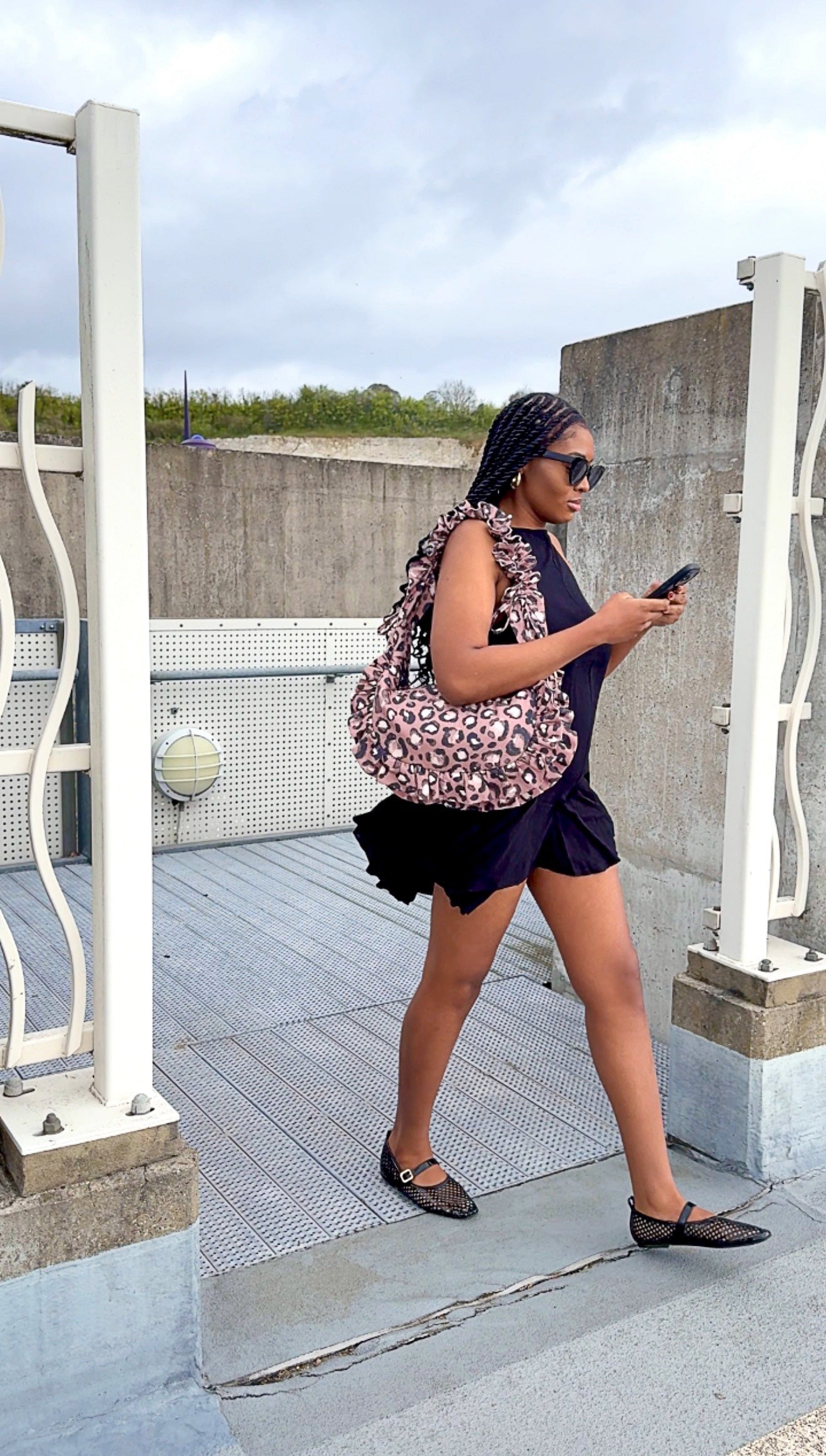Woman in a dark outfit with a taupe brown ruffled crescent handbag on a rooftop.
